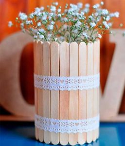 Centro de mesa com flores feito com palito de picolé preso por uma fita de renda
